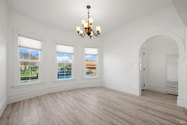 unfurnished dining area featuring arched walkways, a notable chandelier, light wood-style flooring, and baseboards