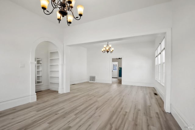 unfurnished room featuring baseboards, light wood-style floors, built in features, and a notable chandelier