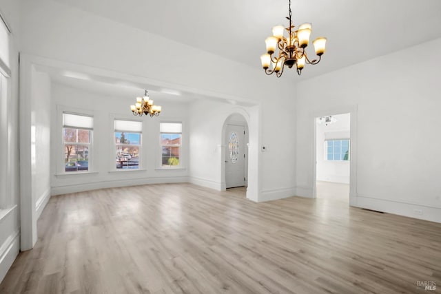 unfurnished living room featuring a chandelier, light wood-type flooring, arched walkways, and baseboards