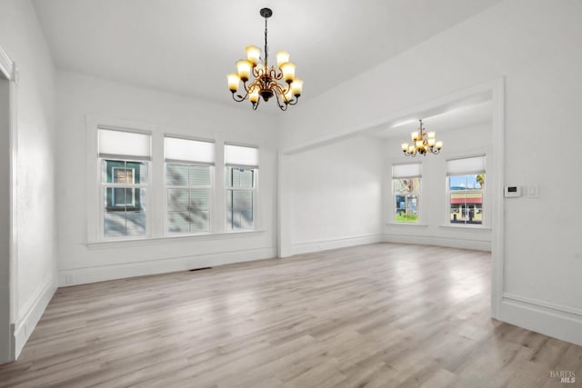 spare room featuring baseboards, light wood-type flooring, and a notable chandelier