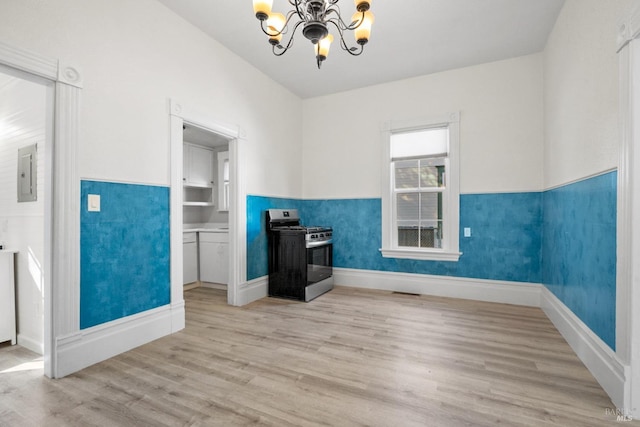 interior space featuring a chandelier, baseboards, light wood-style floors, wainscoting, and electric panel