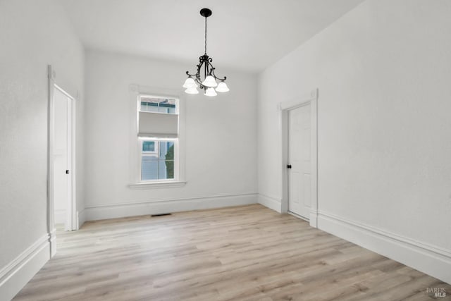 empty room featuring light wood finished floors, baseboards, and a notable chandelier