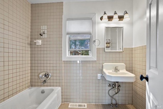 bathroom with a sink, bathtub / shower combination, visible vents, and tile walls