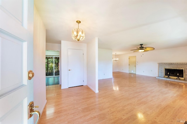 interior space with a brick fireplace, ceiling fan with notable chandelier, and light hardwood / wood-style flooring