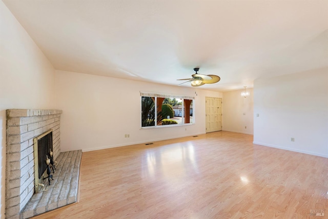 unfurnished living room featuring ceiling fan with notable chandelier, a fireplace, and light hardwood / wood-style floors