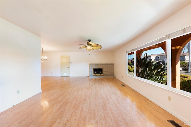 unfurnished living room with a brick fireplace, ceiling fan with notable chandelier, and light hardwood / wood-style flooring