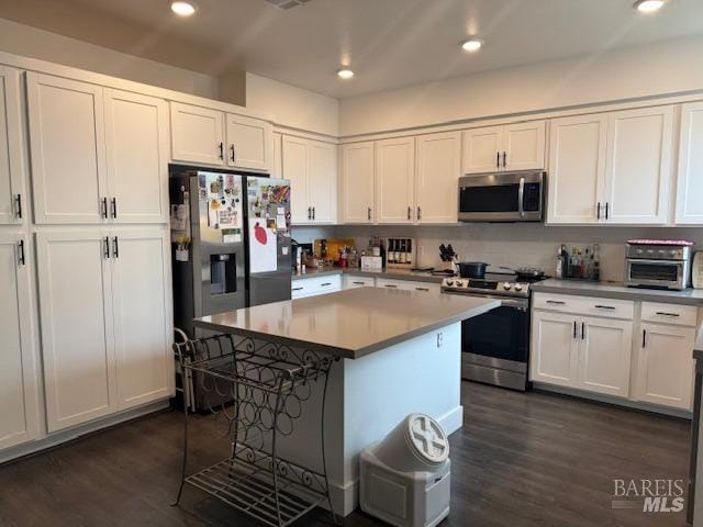 kitchen featuring dark wood-type flooring, a breakfast bar area, a center island, appliances with stainless steel finishes, and white cabinets