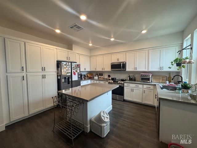 kitchen with stainless steel appliances, a center island, dark wood-type flooring, and white cabinets