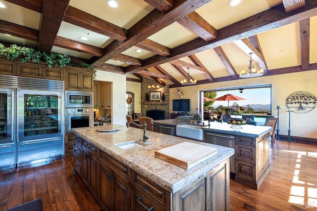 kitchen with sink, stainless steel appliances, a large fireplace, and a center island with sink