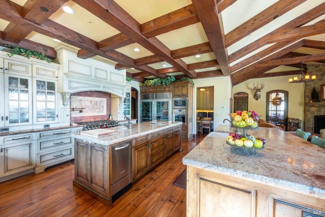 kitchen featuring built in appliances, a large island with sink, a fireplace, light stone countertops, and decorative backsplash