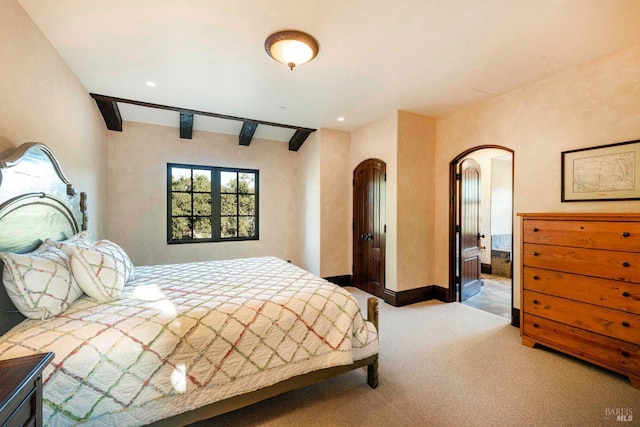 bedroom featuring beamed ceiling, connected bathroom, and light colored carpet