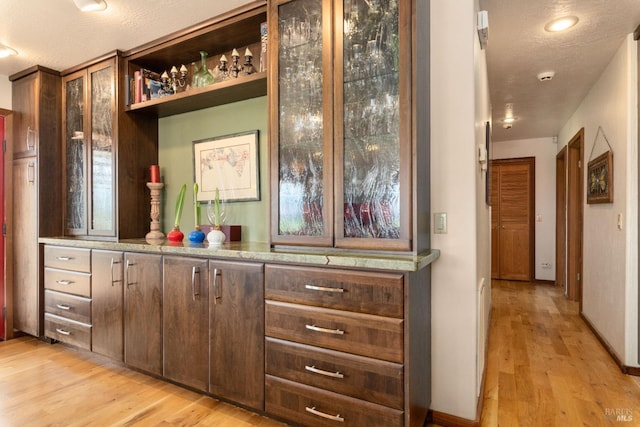 bar with dark brown cabinets, light hardwood / wood-style floors, and a textured ceiling