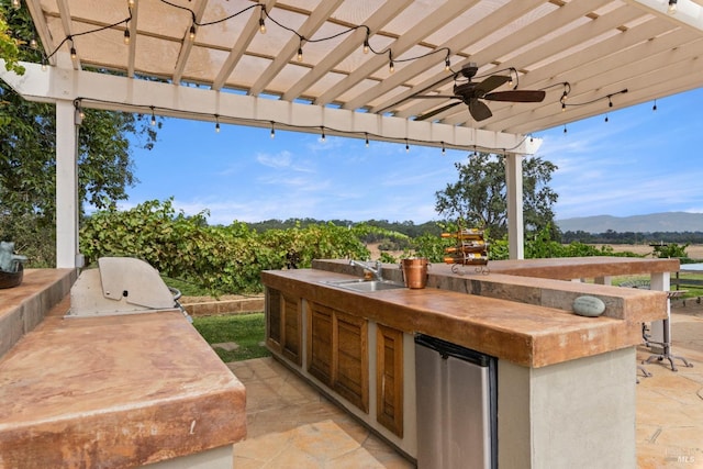 view of patio with sink, ceiling fan, a grill, a mountain view, and exterior kitchen