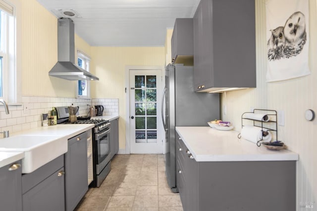 kitchen with appliances with stainless steel finishes, wall chimney exhaust hood, a wealth of natural light, and gray cabinetry