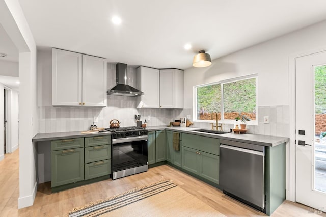 kitchen featuring white cabinetry, wall chimney range hood, sink, and appliances with stainless steel finishes