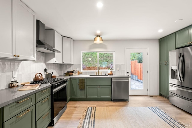 kitchen with wall chimney range hood, sink, green cabinets, stainless steel appliances, and white cabinets