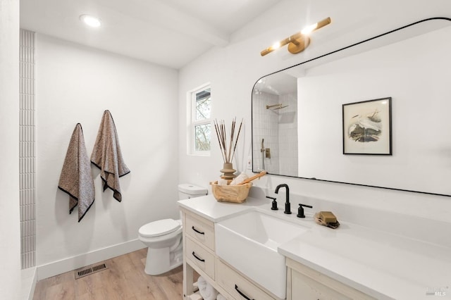 bathroom featuring tiled shower, vanity, wood-type flooring, beamed ceiling, and toilet