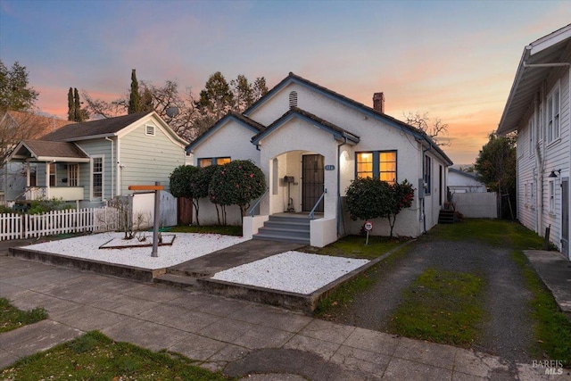 view of front of house with a chimney, fence, and stucco siding