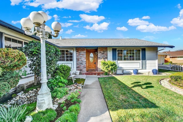 ranch-style house featuring a front yard, brick siding, fence, and a shingled roof