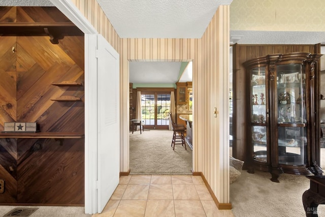 hallway with visible vents, baseboards, a textured ceiling, wallpapered walls, and light colored carpet