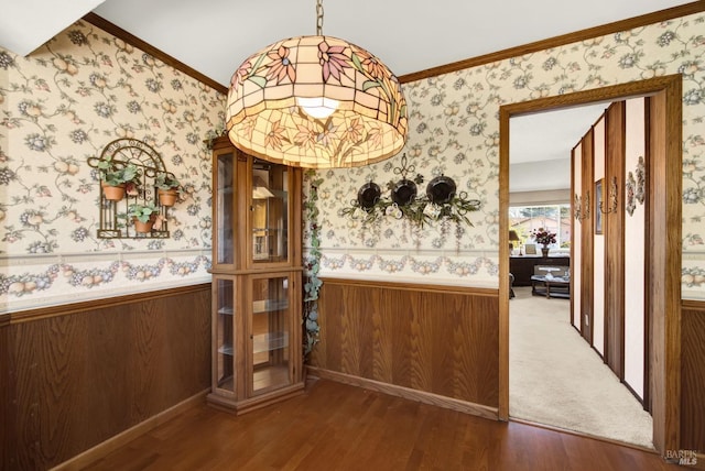 unfurnished dining area featuring ornamental molding, a wainscoted wall, wood finished floors, and wallpapered walls