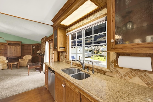 kitchen featuring vaulted ceiling, glass insert cabinets, light stone countertops, dishwasher, and a sink