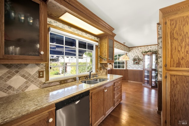 kitchen with a sink, dark wood-style flooring, wainscoting, wallpapered walls, and stainless steel dishwasher