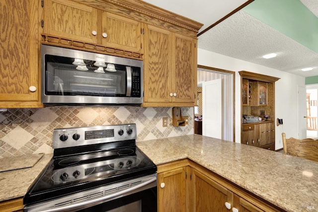 kitchen featuring a peninsula, a textured ceiling, backsplash, brown cabinetry, and stainless steel appliances
