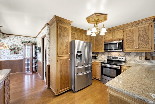 kitchen featuring appliances with stainless steel finishes, a chandelier, wallpapered walls, backsplash, and light wood-style flooring