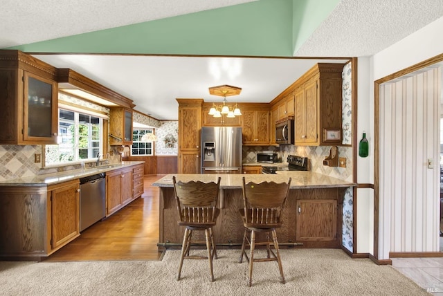 kitchen with glass insert cabinets, a peninsula, appliances with stainless steel finishes, decorative backsplash, and a notable chandelier