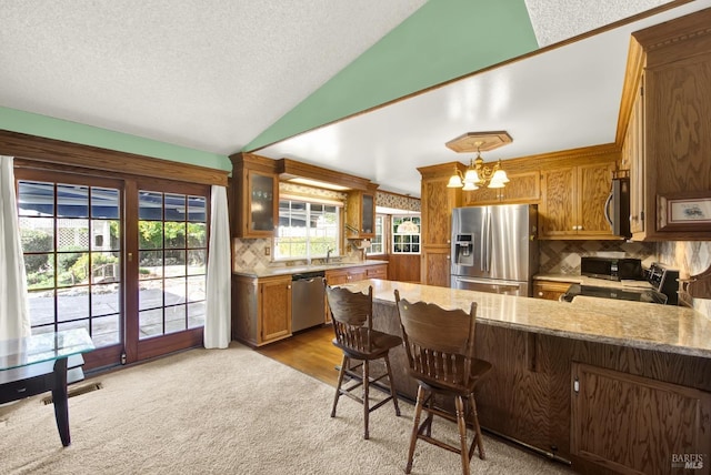 kitchen featuring an inviting chandelier, a peninsula, light colored carpet, appliances with stainless steel finishes, and lofted ceiling