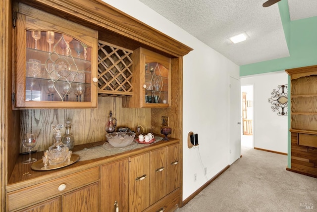 bar with a bar, baseboards, light colored carpet, and a textured ceiling