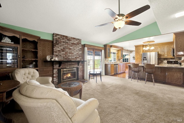 living area with vaulted ceiling, a textured ceiling, a brick fireplace, light colored carpet, and ceiling fan with notable chandelier