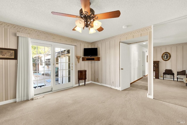 unfurnished living room featuring a textured ceiling, a ceiling fan, carpet floors, wallpapered walls, and baseboards