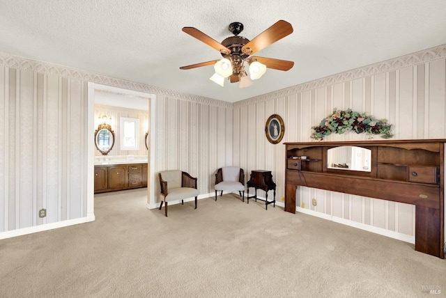 sitting room with baseboards, ceiling fan, carpet, a textured ceiling, and wallpapered walls