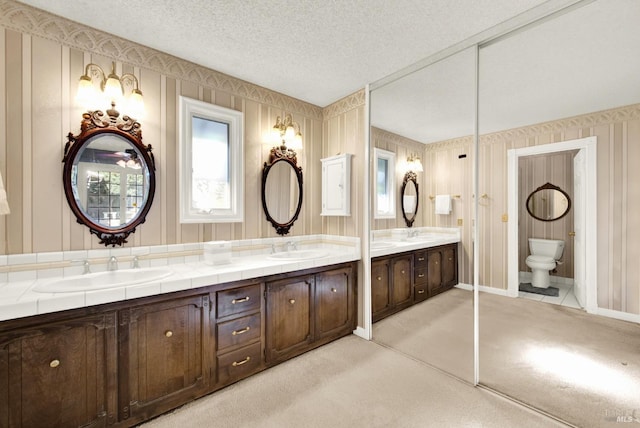 full bathroom featuring toilet, a textured ceiling, double vanity, and a sink