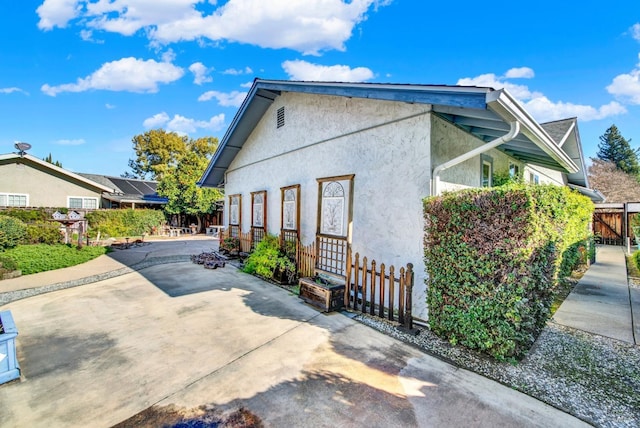 view of side of home featuring a patio area, stucco siding, and fence
