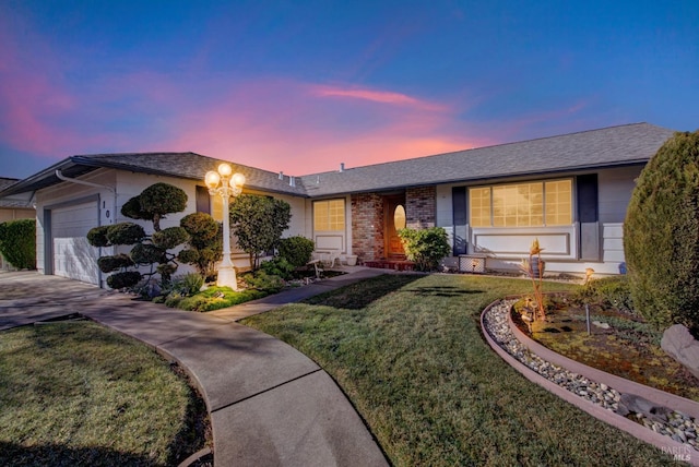 ranch-style home featuring a yard, an attached garage, brick siding, and concrete driveway