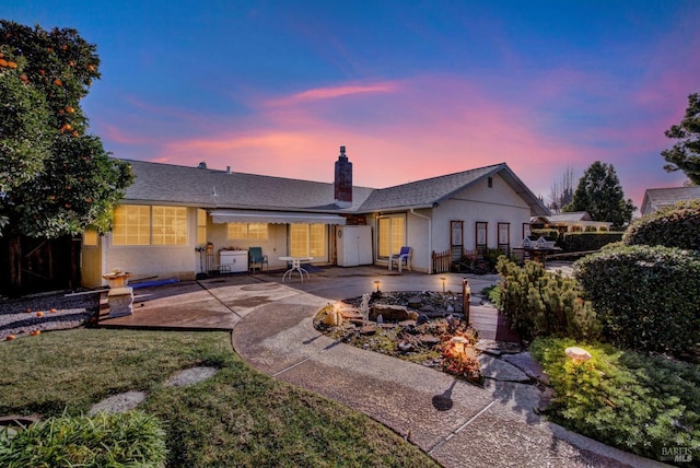 back of house featuring a patio, roof with shingles, stucco siding, and a chimney
