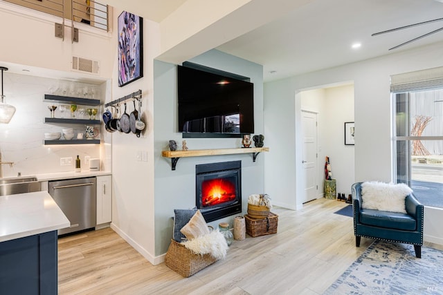 living area featuring light wood-style floors, baseboards, visible vents, and a glass covered fireplace