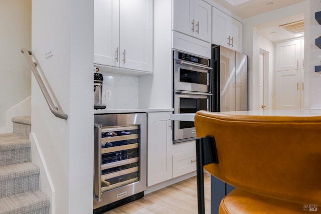 kitchen with light wood finished floors, light countertops, double oven, white cabinets, and beverage cooler