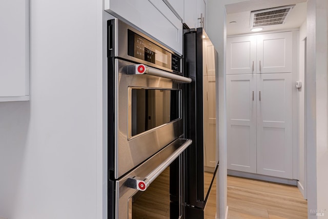 kitchen with stainless steel double oven, light wood-type flooring, visible vents, and white cabinets