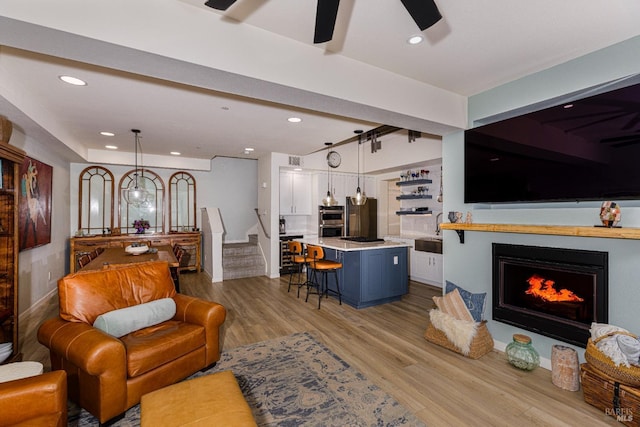 living area with light wood finished floors, ceiling fan, stairway, a lit fireplace, and recessed lighting