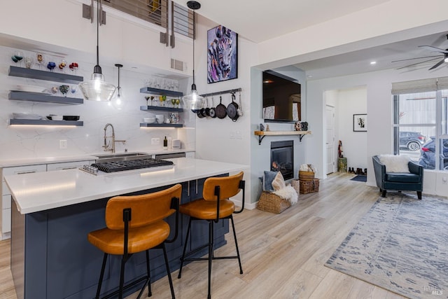 bar featuring light wood-style floors, backsplash, a glass covered fireplace, and pendant lighting