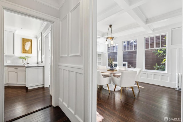 dining space with coffered ceiling, sink, ornamental molding, dark hardwood / wood-style floors, and beamed ceiling