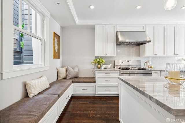 kitchen featuring stainless steel gas stove, white cabinetry, light stone counters, dark wood-type flooring, and wall chimney range hood