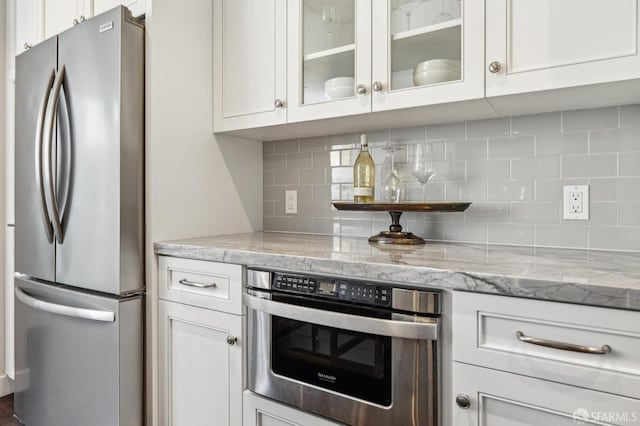 kitchen featuring oven, stainless steel refrigerator, and white cabinets