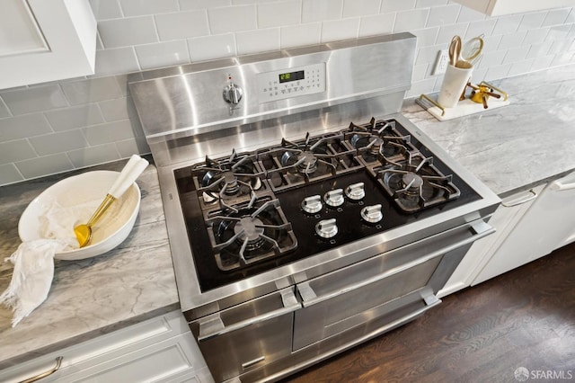 kitchen featuring tasteful backsplash, light stone counters, dark hardwood / wood-style floors, stainless steel range with gas stovetop, and white cabinets