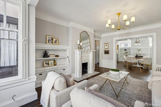 living room featuring dark hardwood / wood-style floors, a notable chandelier, a high end fireplace, ornamental molding, and built in shelves