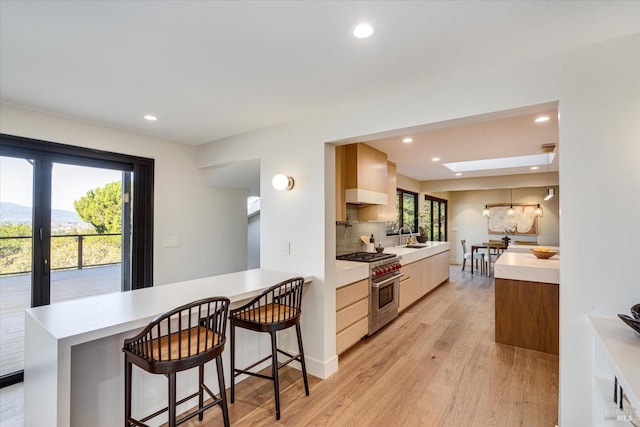 kitchen featuring a skylight, high end stove, sink, a kitchen bar, and light wood-type flooring